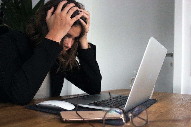 woman in a black long sleeve shirt covering her face with her hands while staring at her laptop